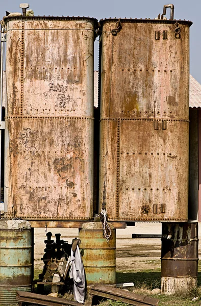Rusted metal tanks balanced on oil drums — Stock Photo, Image
