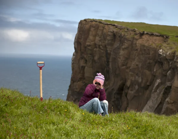 Frau sitzt im Gras auf Klippe der Insel Mykines, Färöer-Inseln — Stockfoto