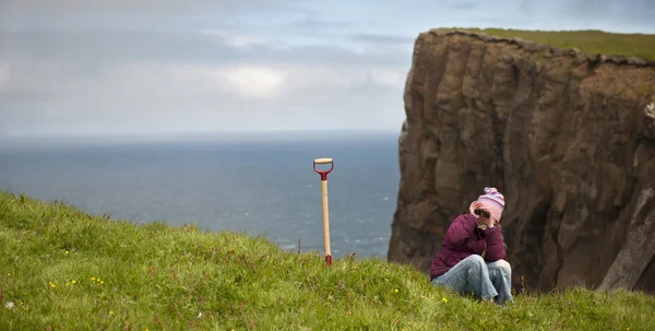 Wanita yang duduk di rumput di tebing pulau Mykines, Kepulauan Faroe — Stok Foto