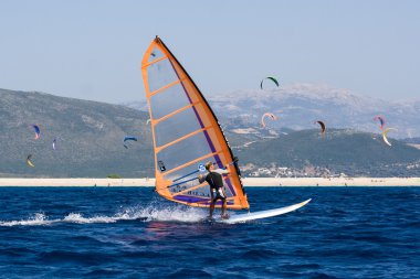 Windsurfing along the coast in the middle of the kite clipart