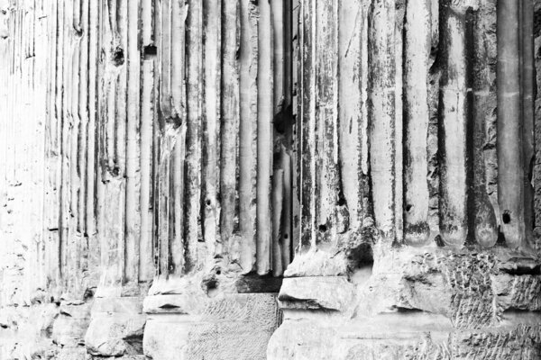 An abstract black and white view of several large stone columns in Rome, Italy.