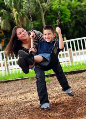 Mother pushing son on swing clipart