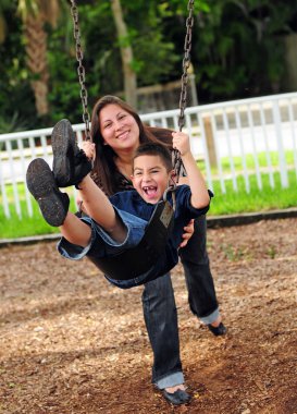 Mom pushing son on swing clipart