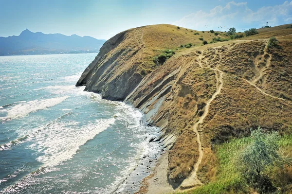 Steep cliff at the edge of the sea, against the backdrop of the Crimean Mountains. — Stock Photo, Image