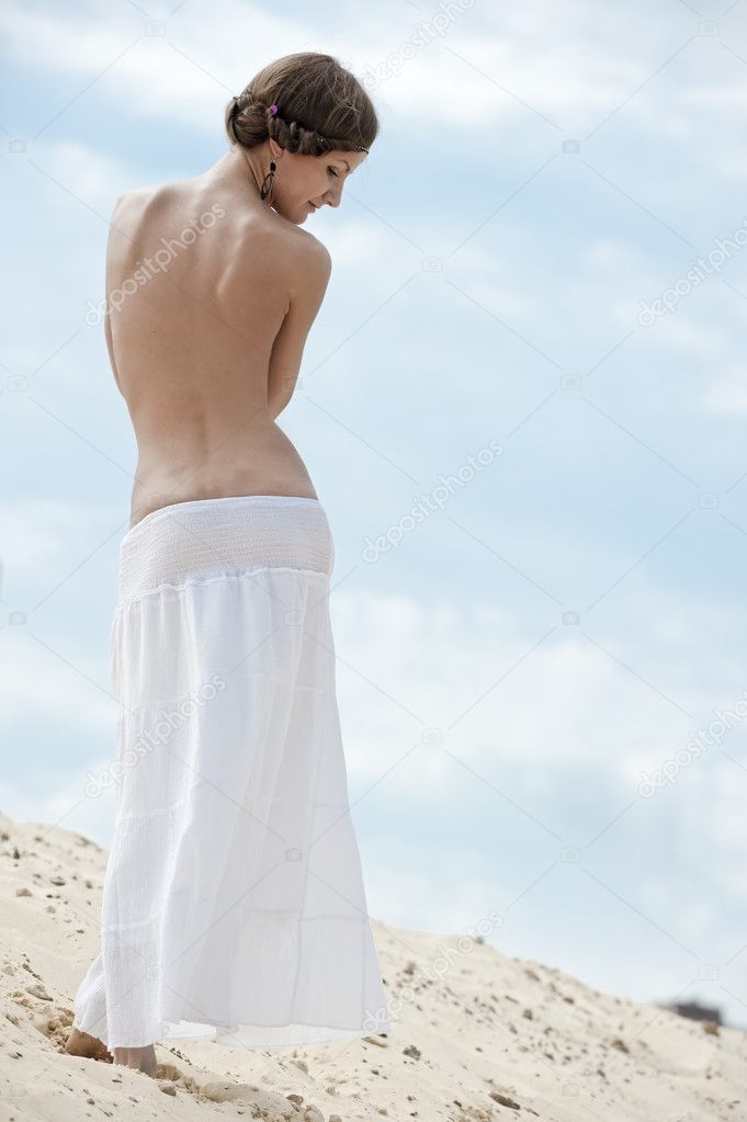 A girl with a bare back is on the sand in the sky