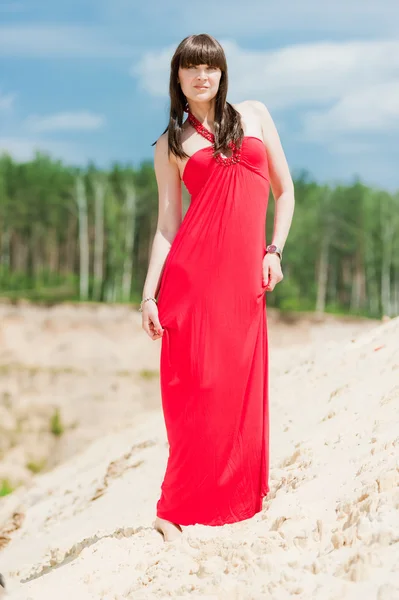 Una chica con un vestido rojo posando en una duna de arena . — Foto de Stock