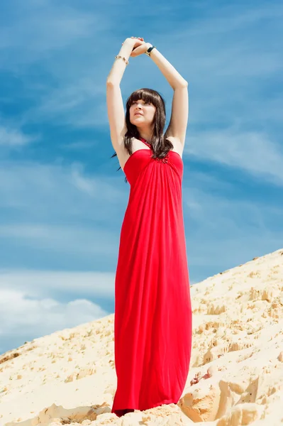 Uma menina em um vestido vermelho posando em uma duna de areia . — Fotografia de Stock