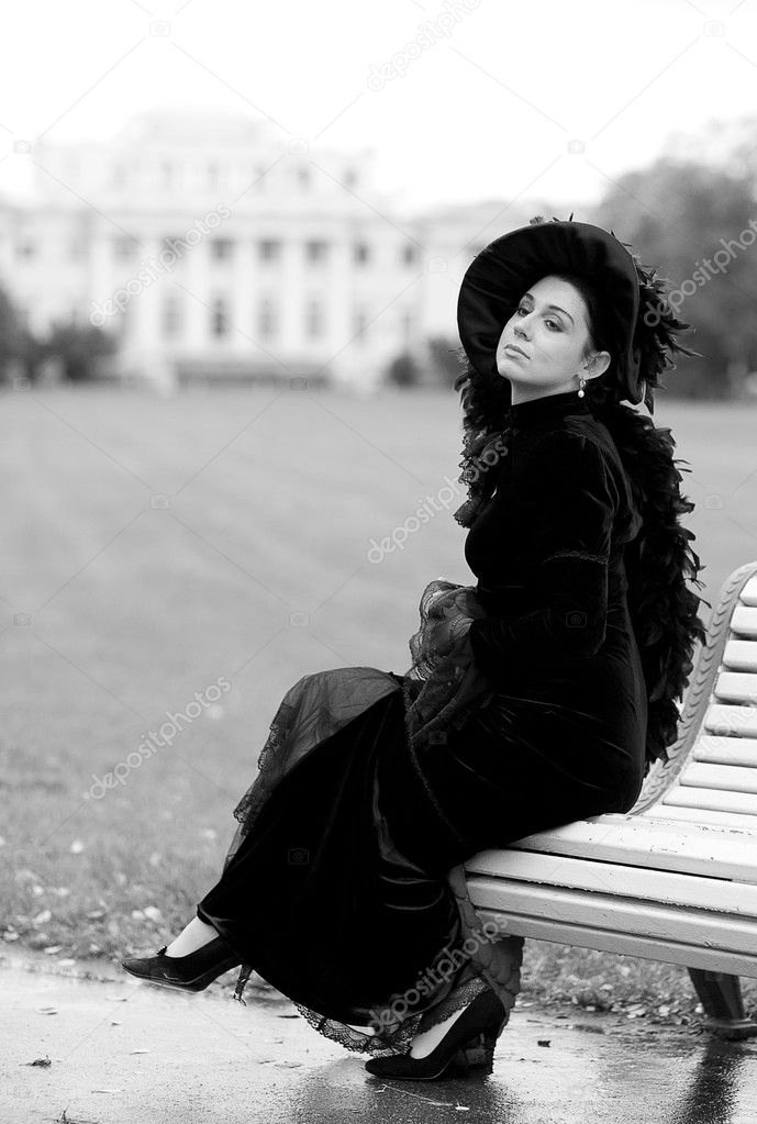 Beautiful aristocratic woman near palace in black dress with cap