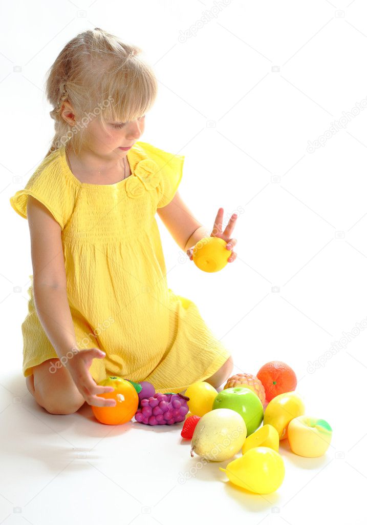 The girl in a yellow dress plays with fruit