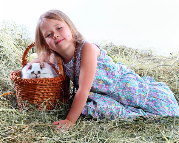Девушка на сене гладит любимого кролика, сидящего в корзине — стоковое фото