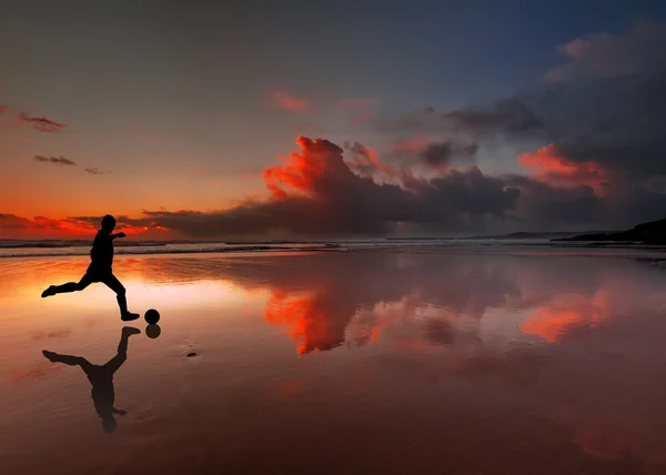 Silhouette of footballer kicking a ball on a beach at sunset — Stock Photo, Image