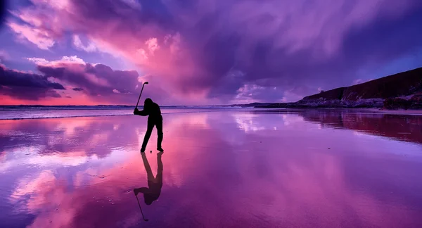 Silhueta de golfista batendo uma bola em uma praia ao pôr do sol — Fotografia de Stock
