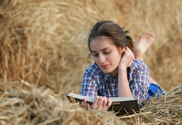Country girl reading book lying at haystack — Stock Photo, Image