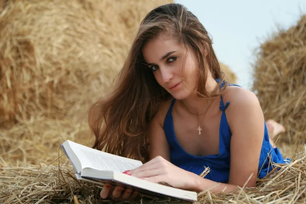 Chica de campo con libro acostado en el pajar mirando a la cámara —  Fotos de Stock