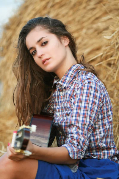 Деревенская девушка с гитарой сидит в стоге сена — стоковое фото