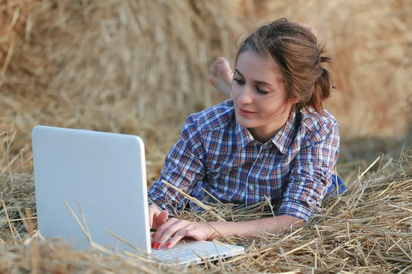 País chica escribiendo en el ordenador portátil acostado en el pajar —  Fotos de Stock