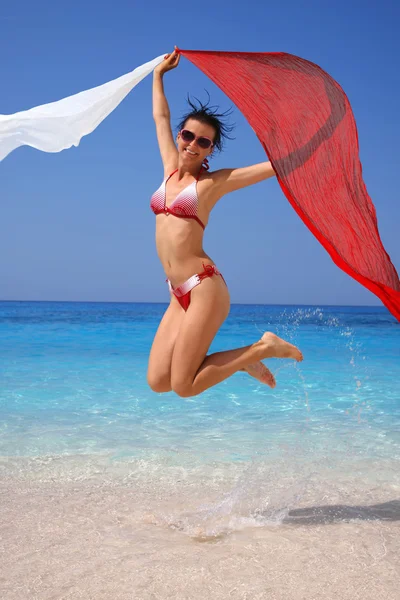 Sexy Frau springt am Strand mit bunten Tüchern — Stockfoto