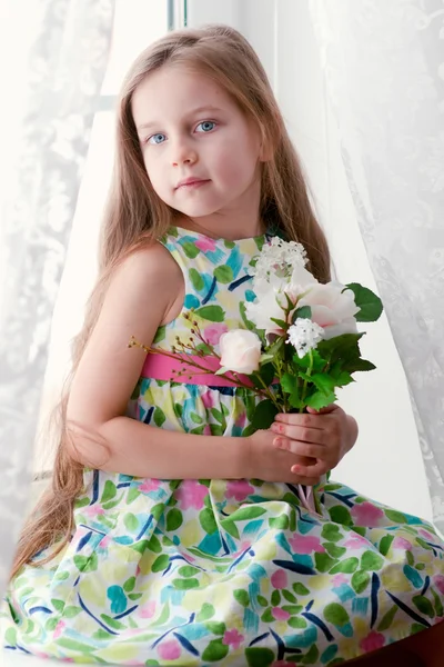 Adorável menina sentada junto à janela com as flores — Fotografia de Stock