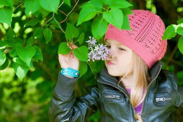 Pretty little girl is smelling flowers in park — Stock Photo, Image