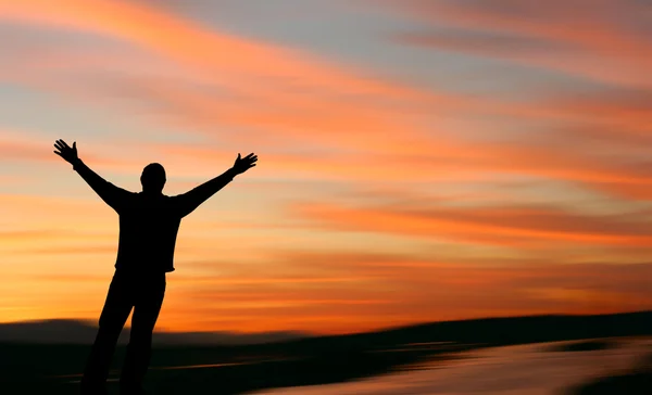 Homem com braços estendidos de frente para um belo pôr do sol — Fotografia de Stock