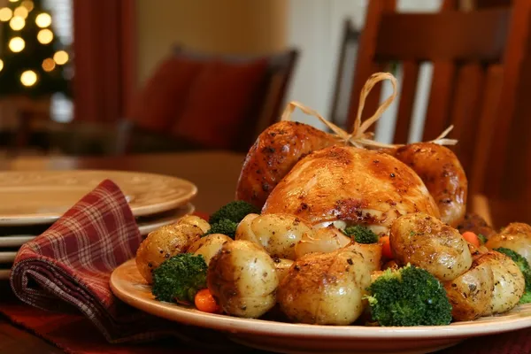 Roast turkey, potatoes, onions, broccoli and carrots, Christmas tree in background — Stock Photo, Image