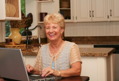 Grand-ma in the kitchen using her laptop clipart