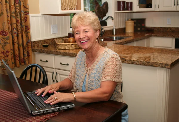 Grand-ma in the kitchen using her laptop — Stock Photo, Image