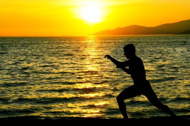 Silhouette of man practicing karate on a sunset beach. clipart