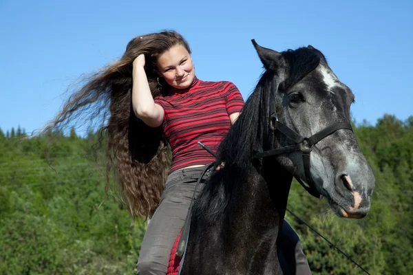 En flicka med hår på en svart häst — Stockfoto