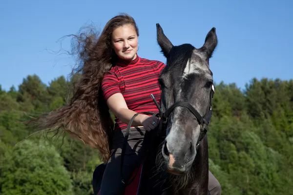 Красивая девушка с каштановыми волосами на черной лошади — стоковое фото