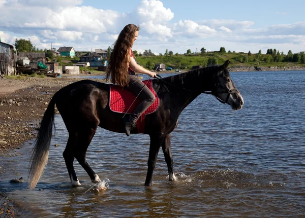 Девушка с распускающимися волосами на черной лошади — стоковое фото