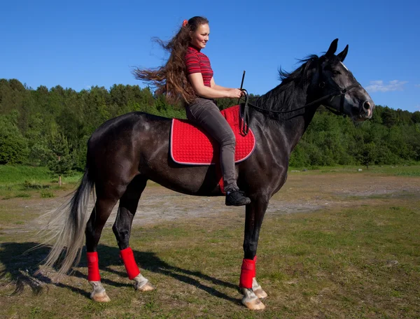 Schönes Mädchen mit braunen Haaren auf einem schwarzen Pferd — Stockfoto