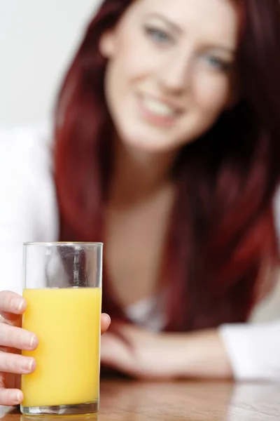 Orange juice glass with woman in background — Stock Photo, Image