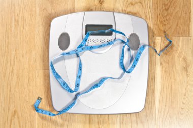 Modern electronic scales with blue tape measure across it clipart