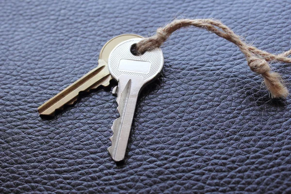 Two keys tied with string on black leather — Stock Photo, Image