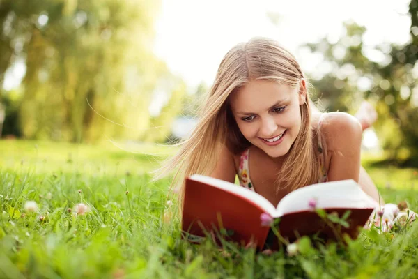 Young woman reading book at park lying down on grass — Stock Photo, Image