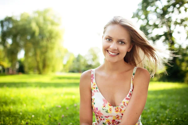Park gülümseyerek, çimlerin üzerine oturan güzel genç kadın — Stok fotoğraf