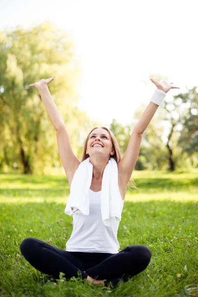 Pretty young woman with arms raised sitting in park — Stock Photo, Image