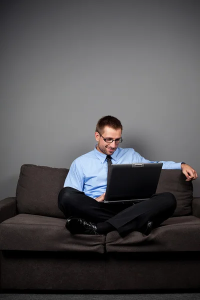 Glad affärsman sitter på soffan med laptop — Stockfoto