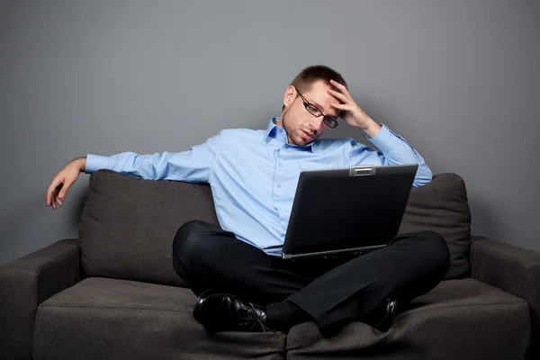 Wyczerpania działalności człowieka na kanapie z laptopem — Zdjęcie stockowe