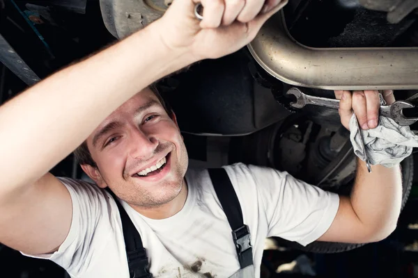 Auto mecánico trabajando bajo el coche sonriendo — Foto de Stock