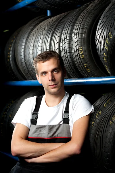Joven mecánico de pie junto a los estantes de neumáticos en la tienda de neumáticos —  Fotos de Stock