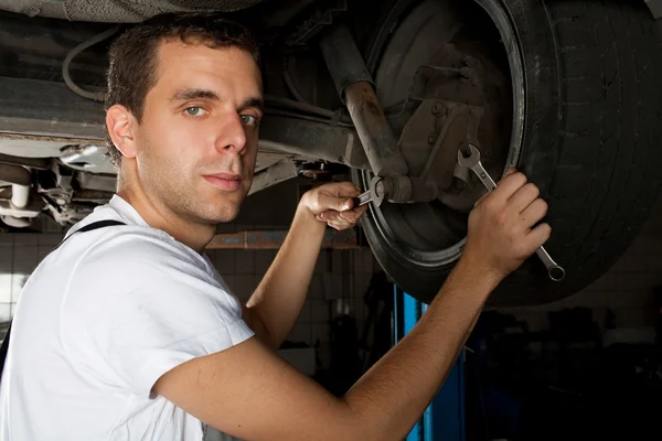Joven mecánico trabajando por debajo del coche con llave inglesa —  Fotos de Stock