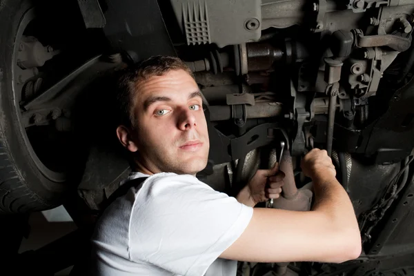 Молодой механик работает под машиной с гаечным ключом — стоковое фото