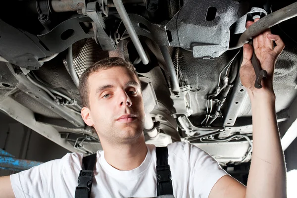 Jovem mecânico trabalhando abaixo do carro em uniforme — Fotografia de Stock