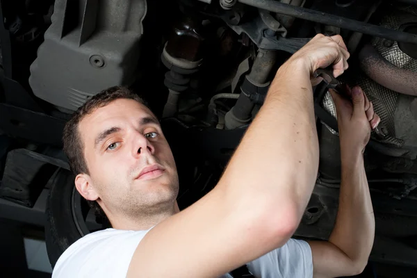 Jovem mecânico trabalhando abaixo do carro com chave inglesa — Fotografia de Stock
