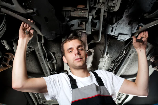 Mekaniker som jobbade under bilen i uniform med skiftnyckel — Stockfoto