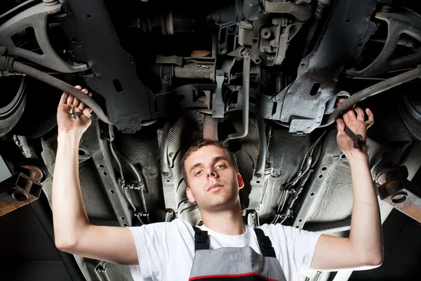 Joven mecánico trabajando debajo del coche en uniforme — Foto de Stock