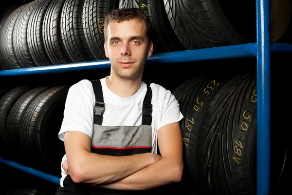 Joven mecánico de pie junto a los estantes de neumáticos en la tienda de neumáticos — Foto de Stock