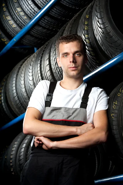 Jovem mecânico em pé ao lado de prateleiras de pneus — Fotografia de Stock
